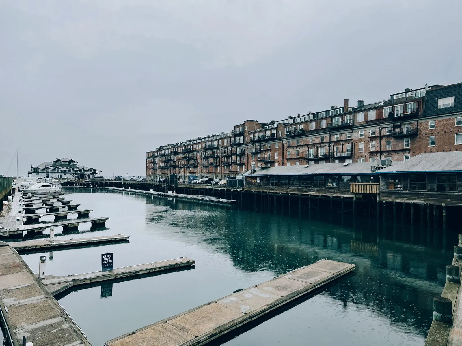 A quiet, overcast day at a harbor with empty docks and a historic waterfront building.